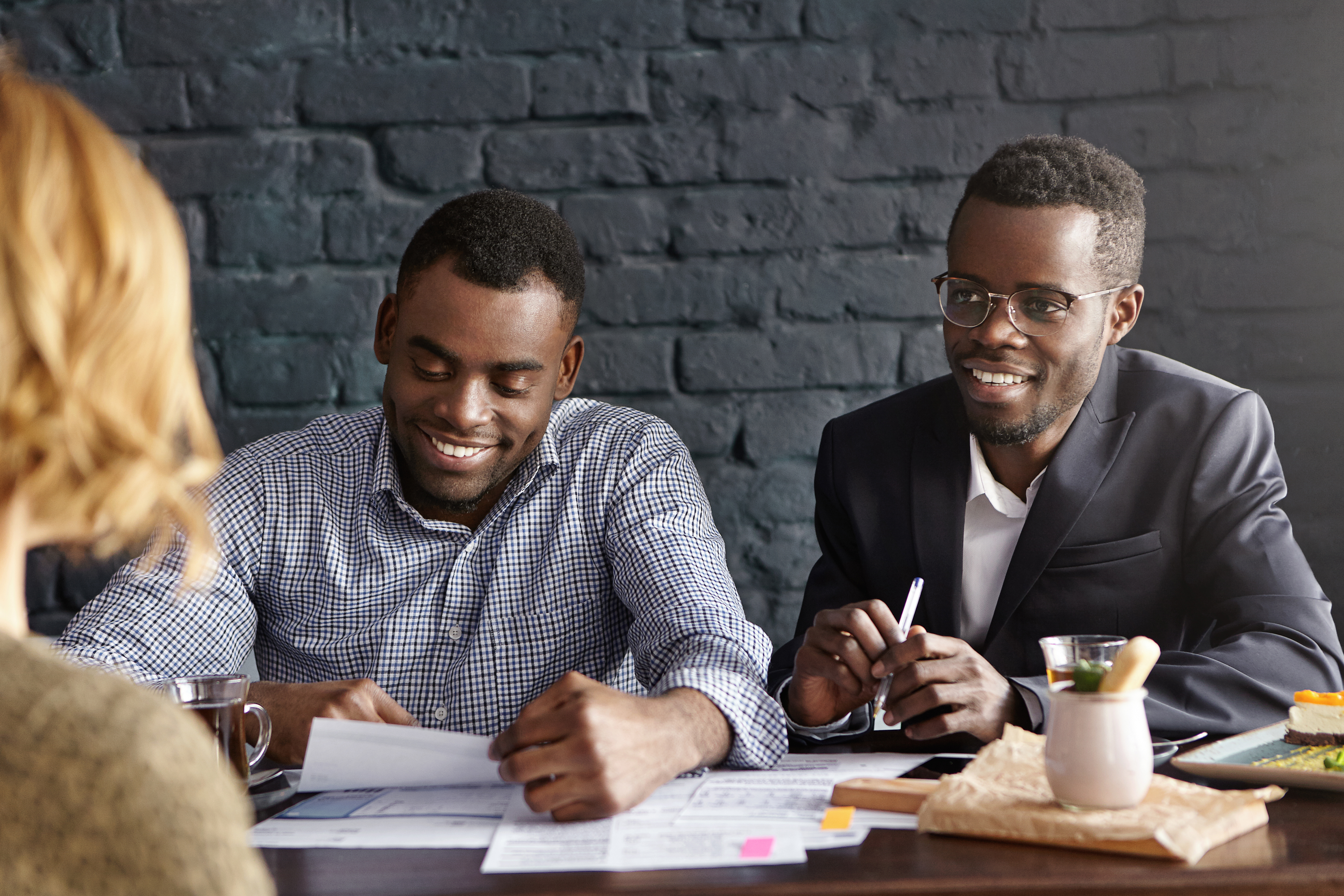 Two dark-skinned employers interviewing young woman with fair hair during job interview. Recruiting expert in suit and his assistant questioning female candidate for position in their company